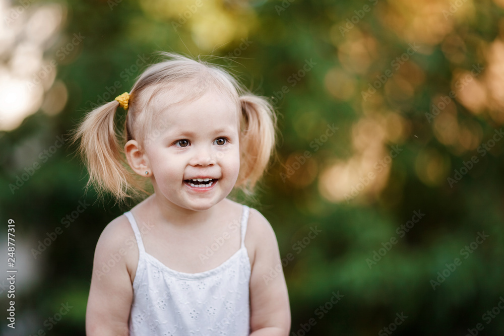 Happy little girl playing in sunny park. Baby girl playing outdoor. Portrait of little girl outdoors in summer Happy little girl playing in sunny park. Baby girl playing outdoor. Portrait of little girl outdoors in summer