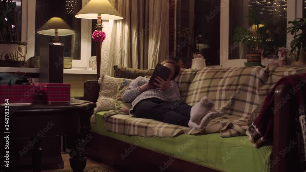 Crane shot. The girl is lying on the sofa and reading an e-book in Crane shot. The girl is lying on the sofa and reading an e-book in