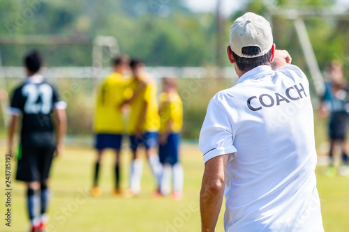Fototapeta Naklejka Na Ścianę i Meble -  Back of male football coach wearing white COACH shirt at an outdoor sport field coaching his team during a game