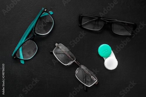 Eye problems. Glasses with transparent lenses and contact lenses on black background top view
