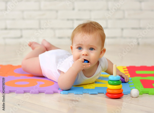 A 7-month-old baby plays on the floor with toys and stuffs small parts into his mouth. Security concept