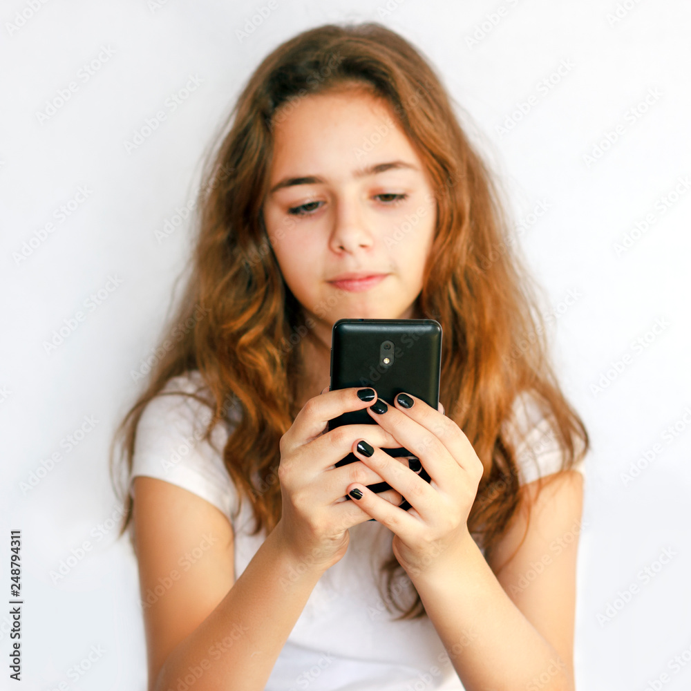 Teen girl holding a black phone in her hands and looking at the screen Teen girl holding a black phone in her hands and looking at the screen