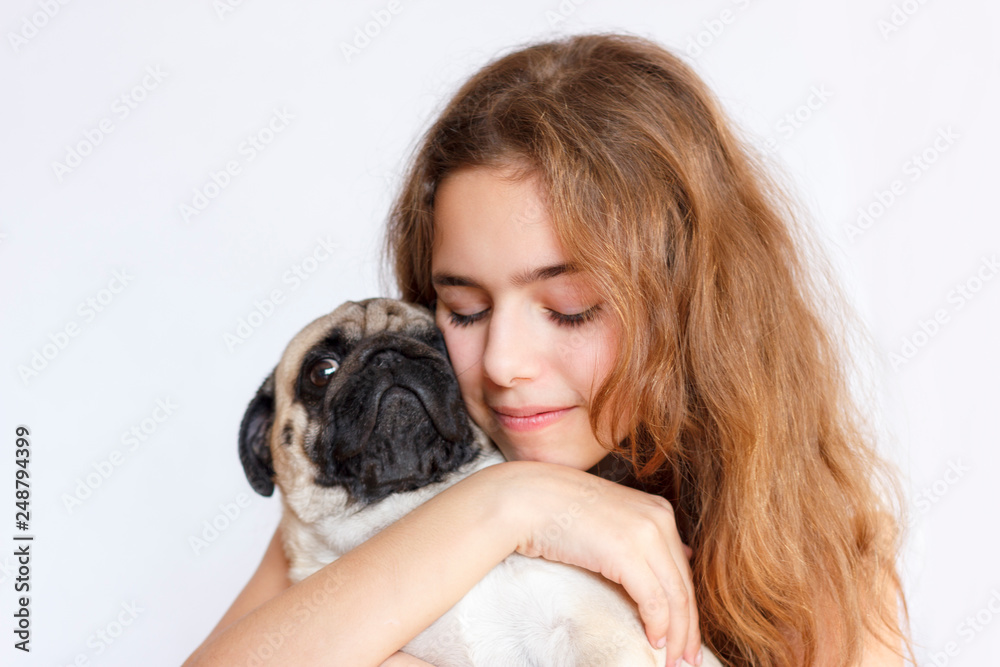 Cute teen girl hugging and kissing a pug dog on white background Cute teen girl hugging and kissing a pug dog on white background