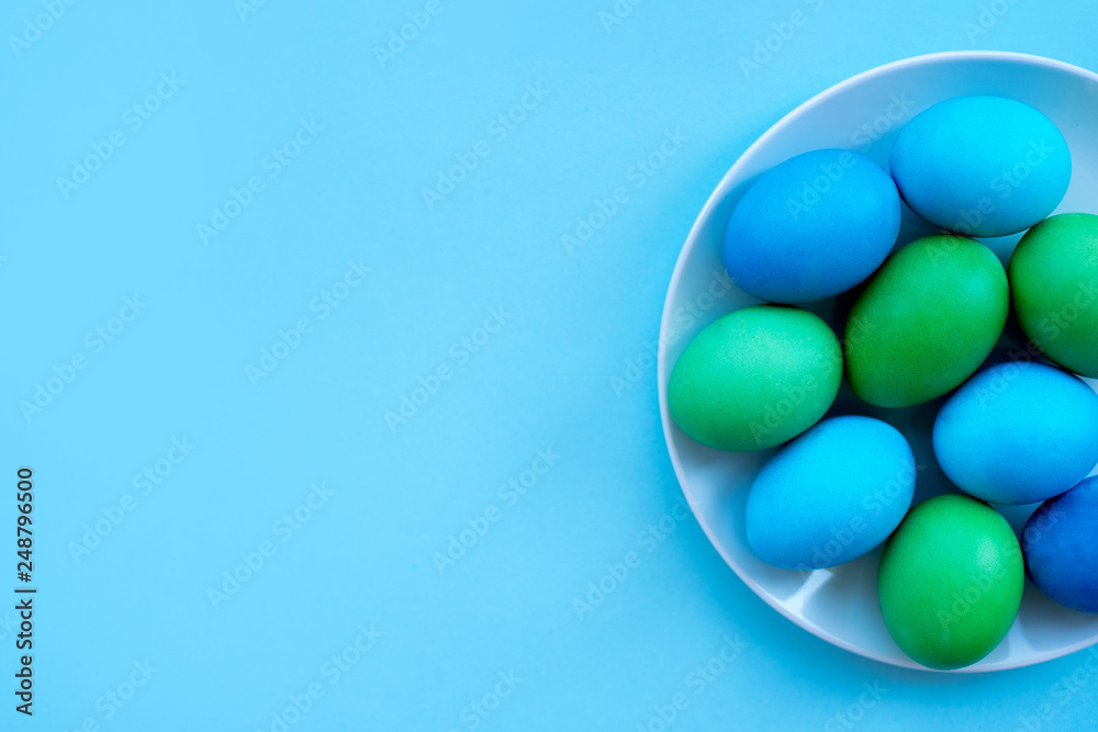 Dyied on green and blue Easter eggs on the white plate flatlay on bright blue background. Hand drawn eggs shot as a flatlay. Dyied on green and blue Easter eggs on the white plate flatlay on bright blue background. Hand drawn eggs shot as a flatlay.