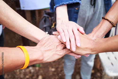 young men and women standing and stacking hands in a meeting on natural ground background at outdoor outing. Teamwork, diversity, collaboration, young generation, harmony, corporate culture concept