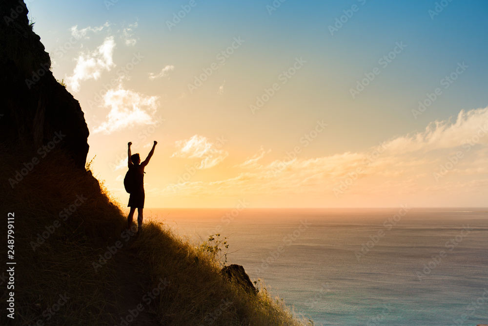 silhouette of man on top of mountain with arms up in the air. 