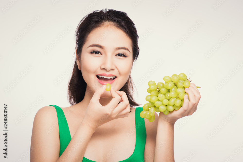 Young beautiful asian woman eating fresh grapes isolated on white background Young beautiful asian woman eating fresh grapes isolated on white background