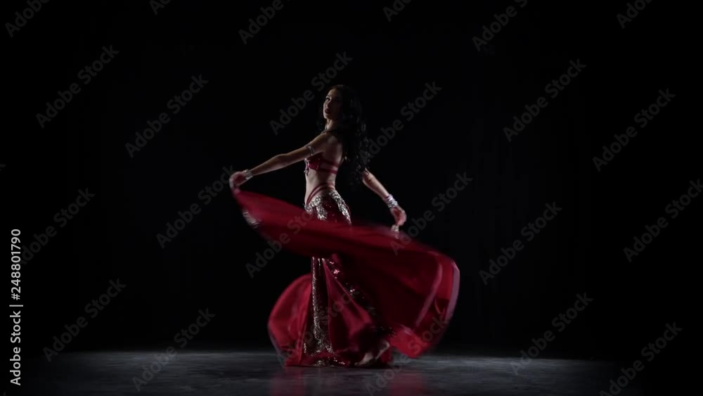 Traditional oriental belly dancer girl dancing in chiffon red dress . Black background