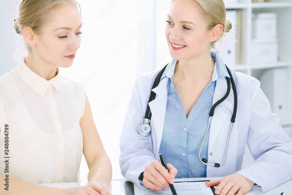 Doctor and patient talking in hospital office while sitting at the desk. Health care and client service in medicine