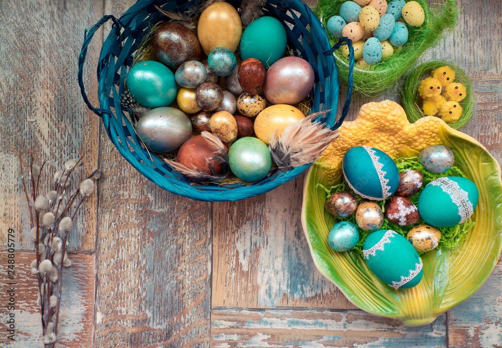 Fototapeta premium On the old wooden shabby table a dish with painted in different colors Easter eggs with feathers willow