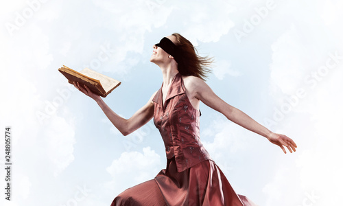Girl against cloudy sky with opened book in palm as idea for knowledge