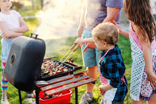 Photos Little chef with apron grilling meat and vegetables on sticks