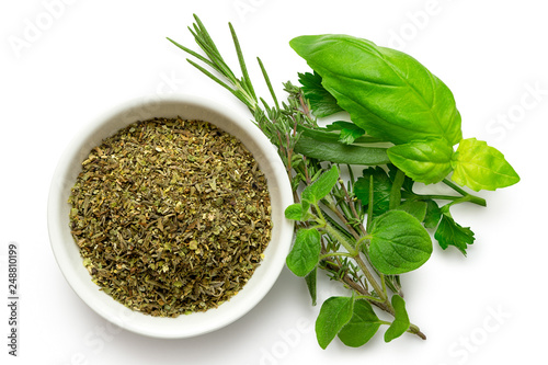 Dried chopped provence herbs in a white ceramic bowl next to fresh bouquet garni isolated on white from above.