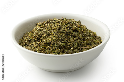 Dried chopped provence herbs in a white ceramic bowl isolated on white.