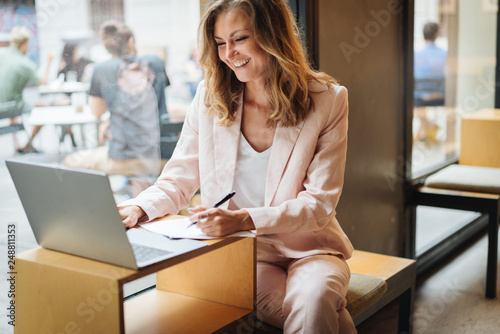 Happy laughing business woman using laptop computer for distant work. Hipster young manager working with notebook in the cafe connected to wireless internet connection, concept of freelance work