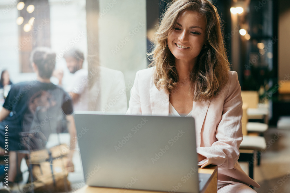 Happy successful business woman having a video call via laptop while sitting in coffee shop, smiling female entrepreneur having a distant meeting or online lesson at computer sitting at cafe Happy successful business woman having a video call via laptop while sitting in coffee shop, smiling female entrepreneur having a distant meeting or online lesson at computer sitting at cafe