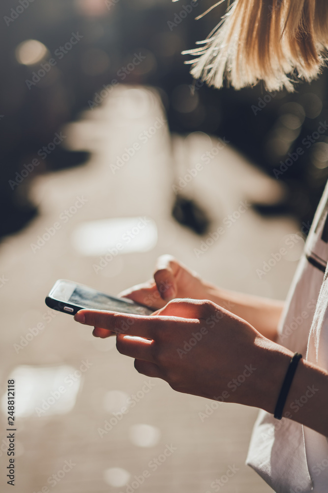 Cropped vertical picture of young girl using internet on her mobile phone while walking on the city streets and enjoying wireless connection talking with friends, focus on hands with cell telephone