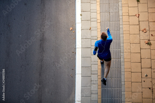 Top view of man running on the street. On arm smart phone. healthy lifestyle concept. © chika_milan
