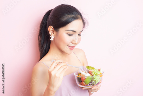 Beautiful Healthy young woman eating salad on pink background
