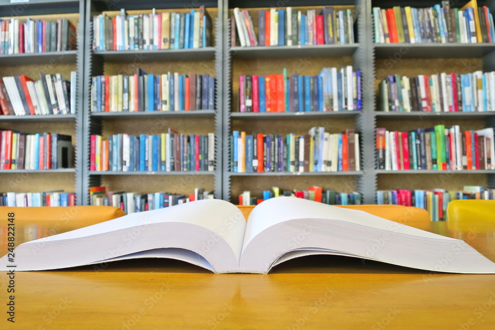The old book open on the wooden table in the library. Selective focus with blurred bookshelves background. Education and book's day concept. The old book open on the wooden table in the library. Selective focus with blurred bookshelves background. Education and book's day concept.