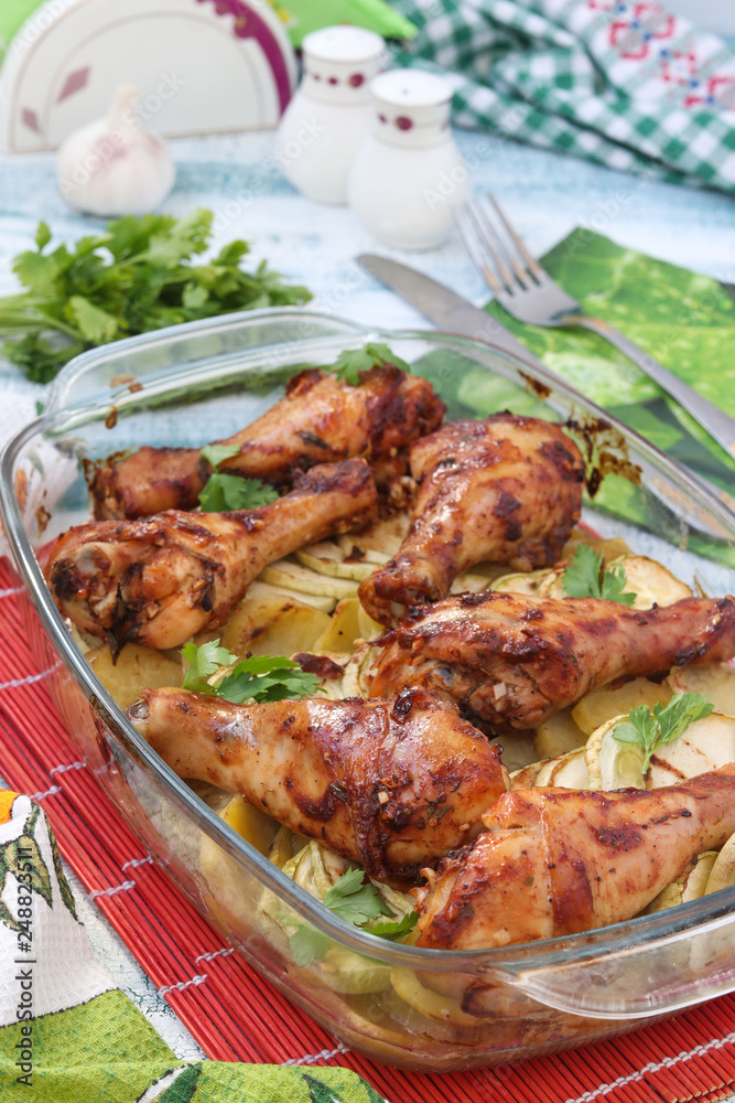 Baked chicken drumstick with potatoes and zucchini in glass form. The photo has a fork, knife and jars of salt and pepper Baked chicken drumstick with potatoes and zucchini in glass form. The photo has a fork, knife and jars of salt and pepper