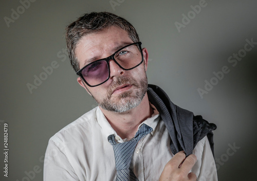 hilarious portrait of 40s weird and wasted businessman in suit and tie wearing ridiculous big broken nerdy glasses posing exhausted feeling a loser isolated on grey background