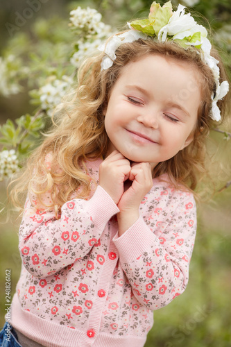 Beautiful little girl outdoors in a blooming spring garden on a sunny day.Little girl in sunny spring. Summer girl fashion. Happy childhood. Springtime. Small child. Natural beauty. Childrens day.