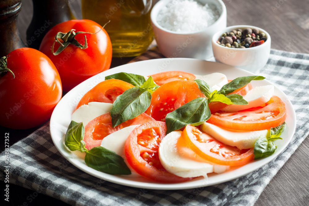 Photo of Caprese Salad with tomatoes, basil, mozzarella, olives and olive oil on wooden background. Italian traditional caprese salad ingredients. Mediterranean, organic and natural food concept. Photo of Caprese Salad with tomatoes, basil, mozzarella, olives and olive oil on wooden background. Italian traditional caprese salad ingredients. Mediterranean, organic and natural food concept.