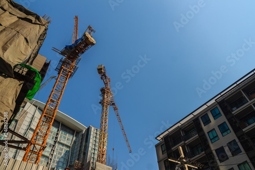 Luffing jib tower crane at condominium construction site over steel framework among high rise building. Skyscraper building construction with the tower cranes on top under the dramatic sky background. © kampwit