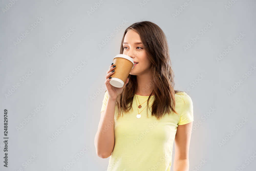 takeaway and people concept - young woman or teenage girl in yellow t-shirt drinking coffee over grey background takeaway and people concept - young woman or teenage girl in yellow t-shirt drinking coffee over grey background