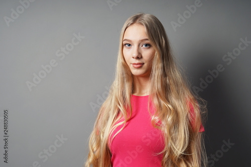 teenage woman with very long blond hair and contented smile against gray background with copy space