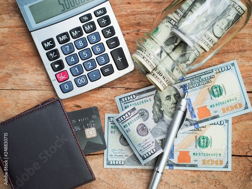 American dollar  banknotes in glass bottle, a credit card in black pocket and calculator on wooden table for money savings concept. photo