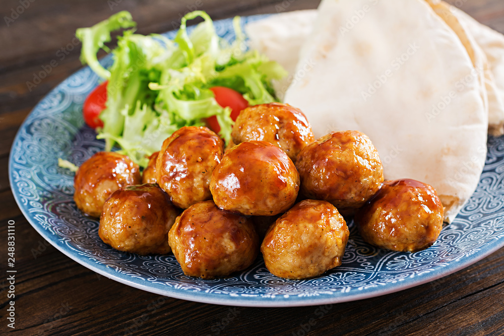 Meatballs in sweet and sour glaze on a plate with pita bread and vegetables in a Moroccan style on a wooden table. Tapas. Trend food. Meatballs in sweet and sour glaze on a plate with pita bread and vegetables in a Moroccan style on a wooden table. Tapas. Trend food.