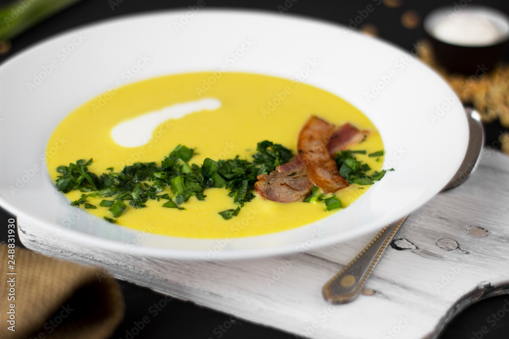Pea soup with pieces of bacon, parsley and onion in a bowl on a dark background. Pea cream soup. Macro. Pea soup with pieces of bacon, parsley and onion in a bowl on a dark background. Pea cream soup. Macro.