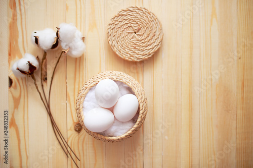 White eggs and eggs in foil on the wooden background with flowers and cotton around. Eggs in the basket