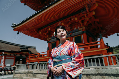 local japanese girl smiling walking praying in kiyomizu dera temple kyoto japan. young woman in floral kimono dress walking standing in ground of tall tower pagoda in background. religion concept. © PR Image Factory