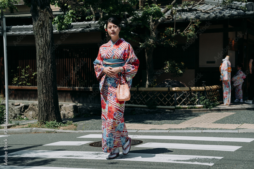 full length of young beautiful asian chinese tourist wear kimono cross the road walking on street. japanese traditional cloth shop renting service in kyoto japan. model in colorful dress front door