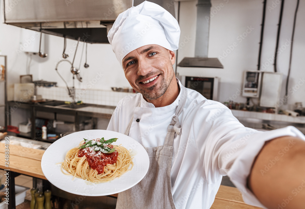 Image of happy man chief in apron taking selfie, while standing at kitchen in restaurant Image of happy man chief in apron taking selfie, while standing at kitchen in restaurant