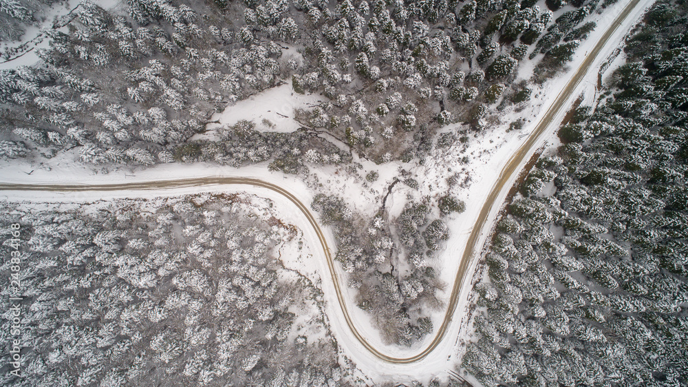 Aerial view of a road in idyllic winter landscape. Country road going through the beautiful snow covered landscapes. 