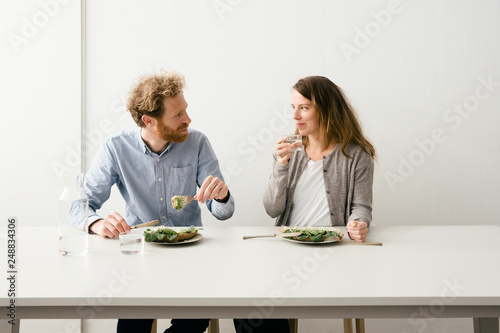 Thirty something European couple sitting down for a avocado sandwich lunch together looking at each other.