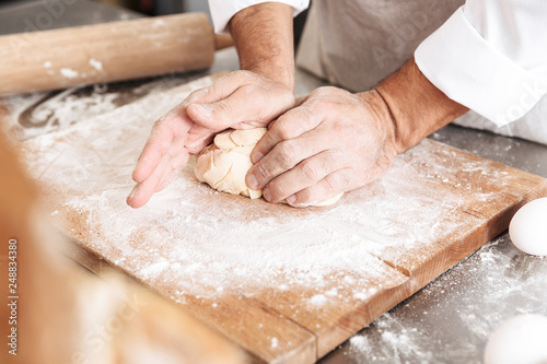 Сropped portrait of male hands mixing dough for pastry, on table at bakery or kitchen