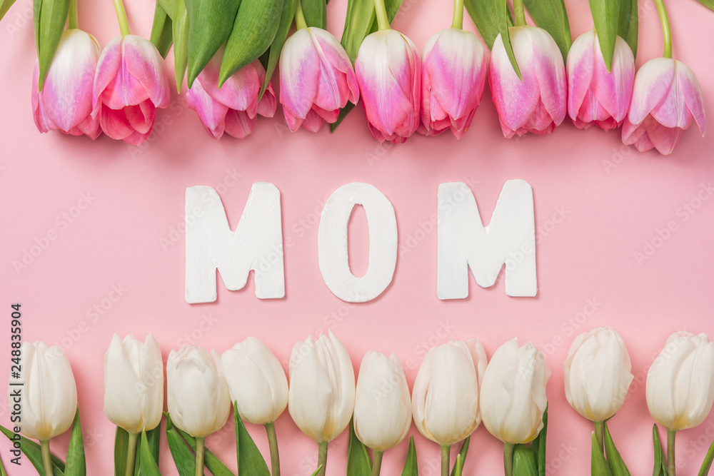 pink and white tulips arranged in rows with paper word mom in center on pink background