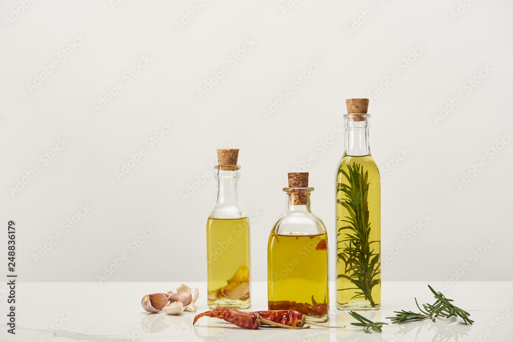 bottles of oil flavored with rosemary and various spices on white surface