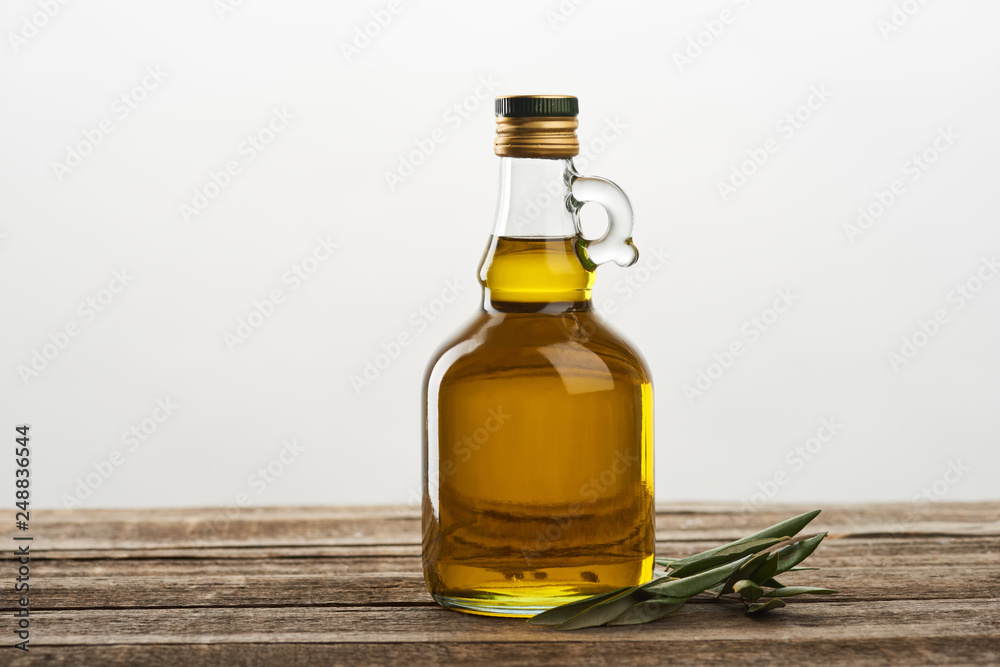 bottle of olive oil and olive tree leaves isolated on grey