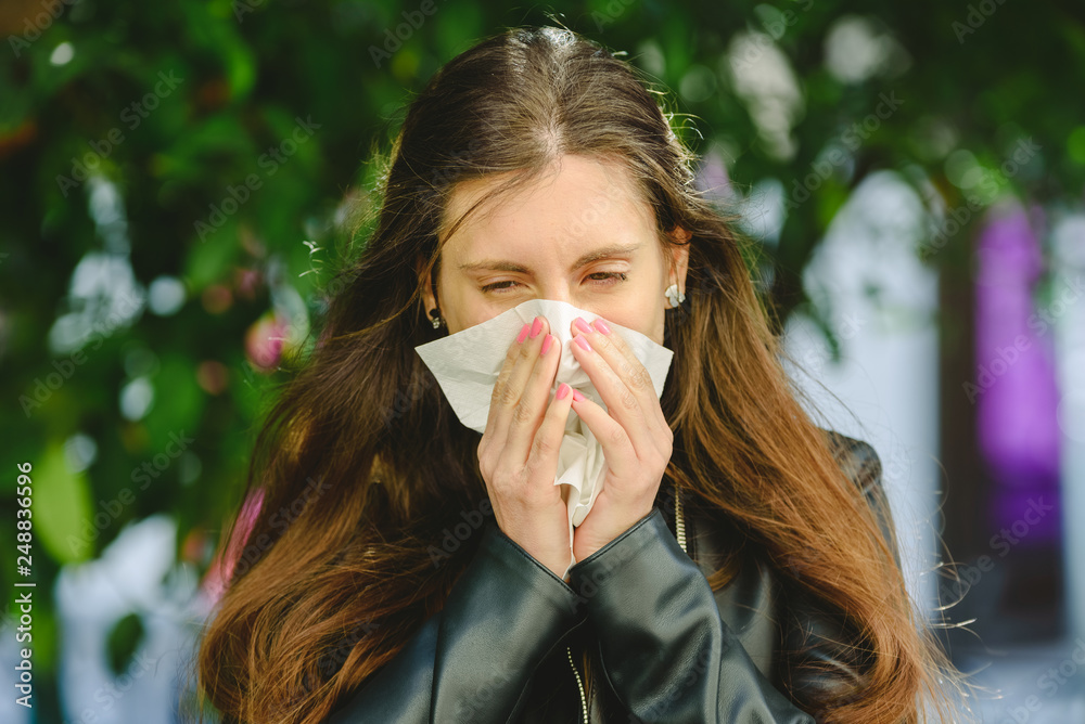 Young woman blowing her nose affected by spring allergy to pollen in a garden, with sinus problems Young woman blowing her nose affected by spring allergy to pollen in a garden, with sinus problems