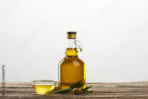 bottle and bowl with oil, olives and olive tree leaves isolated on grey