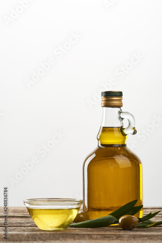 bowl and bottle of oil, olive tree leaves and olives isolated on grey