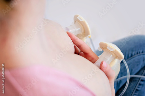 Young mother is using double electric breast milk pump and pumping breast milk for her baby. - image photo