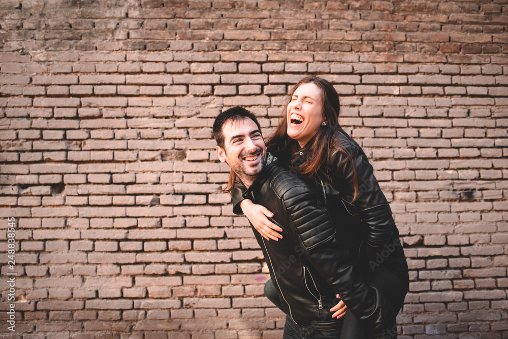 Girl riding on the back of her boyfriend laughing and having fun together as they look young and happy.