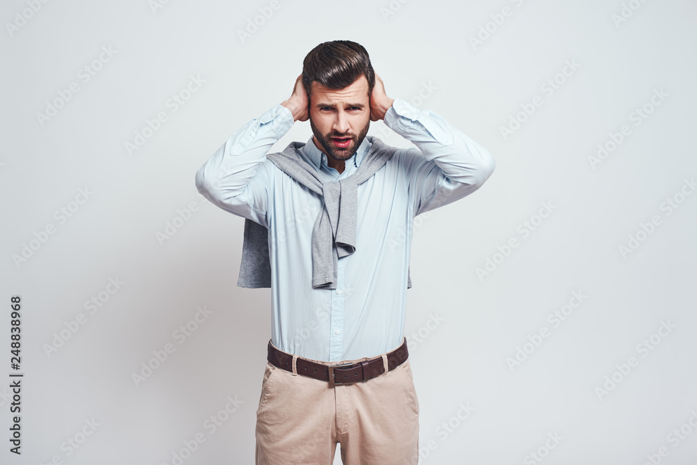Stop saying! Close-up portrait of young annoyed man closing ears with hands while standing in studio on a grey background. Stop saying! Close-up portrait of young annoyed man closing ears with hands while standing in studio on a grey background.